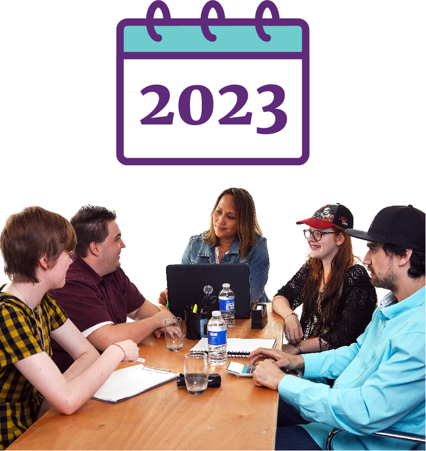 A group of people sitting around a table and talking. There is a calendar that says '2023'.