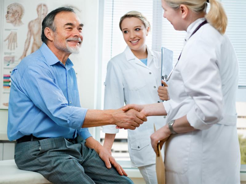 A person meeting with 2 doctors. One of the doctors is shaking the person's hand.