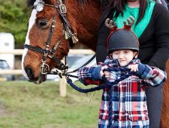 A photo of a child wearing a horse riding helmet next to a horse. 